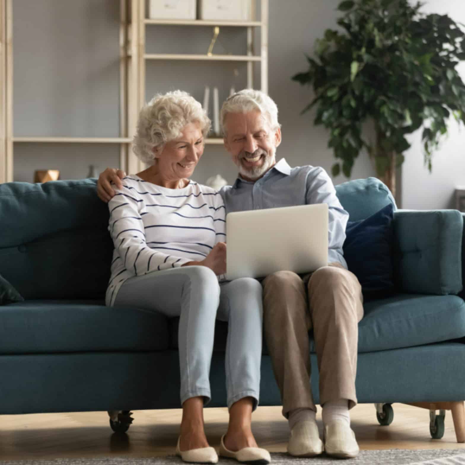 An older couple sitting together on a couch while looking at their laptop screen together